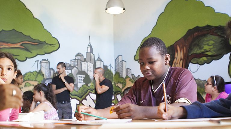 Des enfants installés autour d'une table d'une antenne jeunesse de Pantin dessinent et discutent 